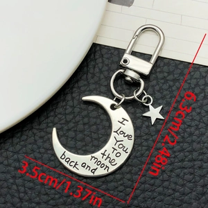 Détail du porte-clés lune argenté avec gravure et breloque étoile sur fond en cuir noir