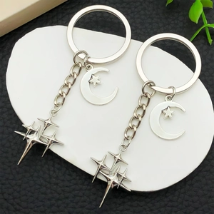 Silver crescent moon and star alloy keychains displayed on white platform over black leather