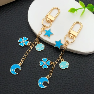 Golden keychain featuring blue enamel star, moon, clover, and cloud pendants on black leather