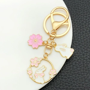 Close-up of golden cherry blossom rabbit keychain with pink enamel details on dark background