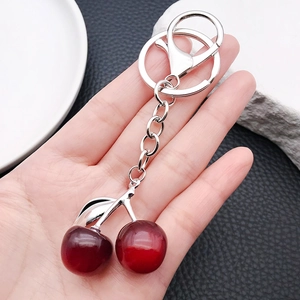 Cute red resin cherry keychain with silver leaves held by hand over a white plate