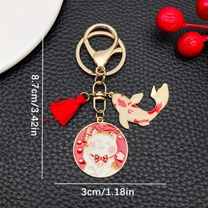 Golden Maneki Neko keychain with red silk tassel and lucky koi fish charm on black background