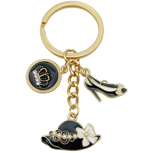 Porte-clés doré avec couronne, chaussures à talons et chapeau à perles sur fond blanc