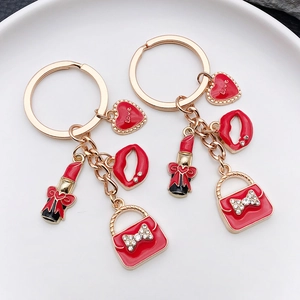 Portachiavi dorato con ciondoli in smalto rosso a forma di cuore, rossetto e borsa