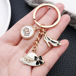 Golden keychain featuring crown charms, high heels, and pearl hat pendants on a hand