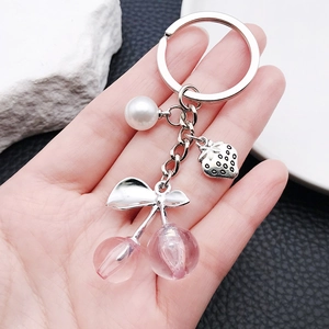 Pink resin cherry keychain with silver strawberry leaf and pearl charm on hand
