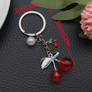 Creative transparent red resin cherry keychain with white pearl on a black leather background
