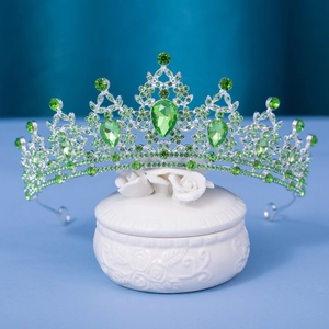 Elegant silver bridal crown with green crystals on white ceramic box and blue background