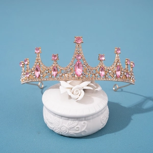 Elegant gold bridal tiara with pink crystals and rhinestones on a white ceramic display