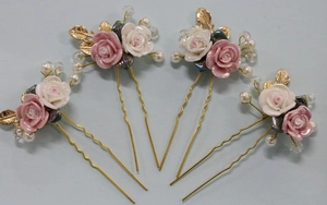 Macro detail of four gold bridal hair pins with pink ceramic roses and pearls