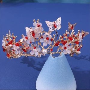 Close-up of golden bridal crown featuring red rhinestones, white flowers, and butterflies
