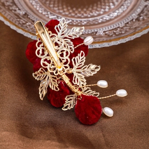 Détail de la pince à cheveux camélia rouge avec feuilles dorées et perles sur soie