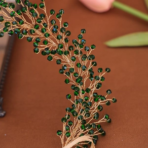 Macro detail of handmade gold wire hairpiece with faceted deep green crystal beads