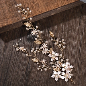 Close-up of golden bridal hair vine with white pearls and metal flowers on wood