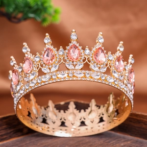 Baroque gold crown with pink crystals and white diamonds on a dark wooden tray