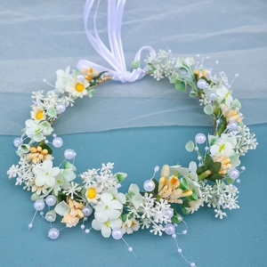 Detail view of ivory floral crown with green leaves, pearls, and long white ribbons