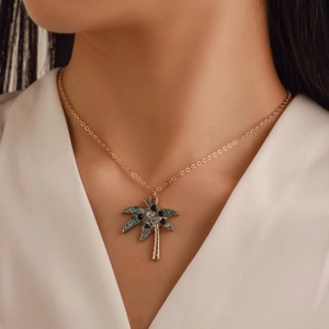 Detail of a gold palm tree pendant necklace with blue and white crystals on a model
