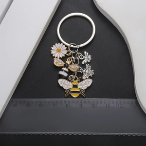 Enamel bee and daisy keychain with rhinestones and silver metal charms on black background