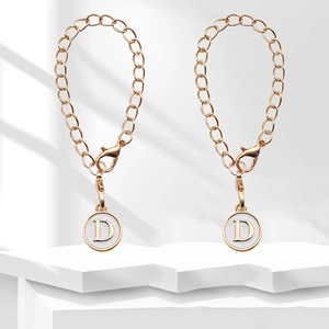 Detail of golden chain charm with white enamel disk featuring a gold letter D pendant