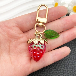Cute red resin strawberry keychain with golden leaves and sparkling pink sequins on white