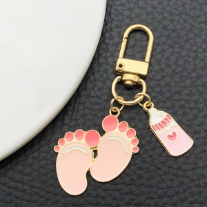 Pink enamel baby footprint and bottle charms on a gold keychain with black leather background