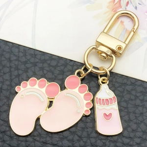 Detail of pink enamel baby feet and bottle charms on a gold U-shaped keychain