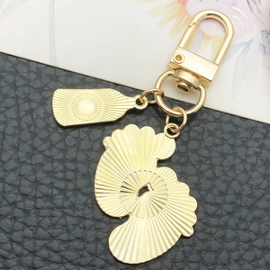 Golden metal keychain with shell charm and engraved rectangle tag on black leather background