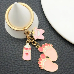 Detail of pink baby onesie, bottle, and tiny footprints on a gold metal keychain