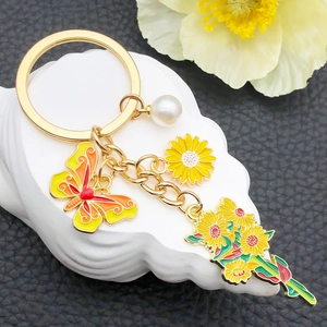 Yellow sunflower and butterfly keychain charm with pearl on a textured white surface