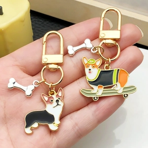 Cute enamel Corgi dog keychains with gold D-rings and silver bone charms in hand