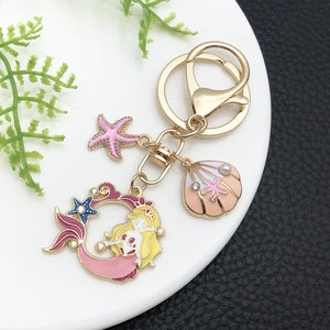 Détail des breloques sirène et étoile de mer en émail rose sur un porte-clés doré
