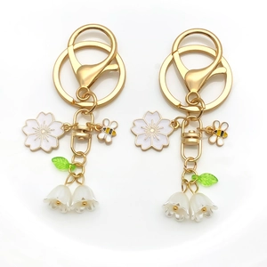 Détail d'un porte-clés doré avec fleurs de cerisier blanc, muguet et breloques abeilles