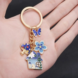 Creative gold keychain featuring blue butterfly, flower, and mushroom house enamel charms