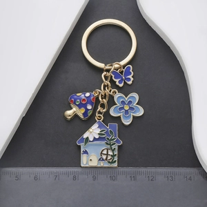 Detailed view of enamel flower and mushroom house charms on a gold keychain with ruler