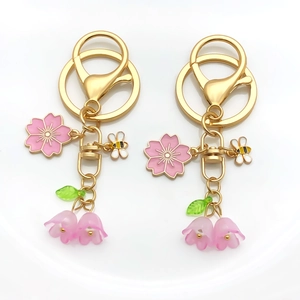 Detailansicht der goldenen Schlüsselanhänger mit rosa Emaille-Blumen und Bienenmotiven