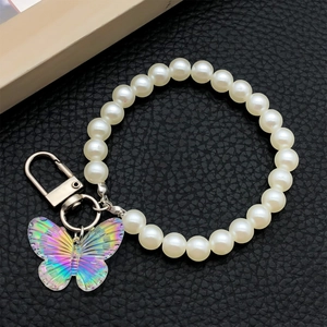 Detail of white pearl wrist strap with iridescent acrylic butterfly charm and metal clasp