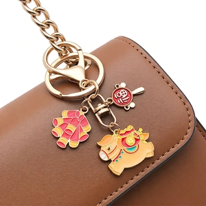 Detail of a golden zodiac horse keychain with red firecrackers on a leather bag