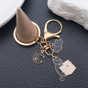 Detail view of cartoon black cat reading a book keychain with moon and cloud charms