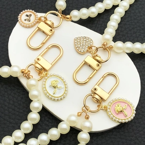 Faux pearl keychain with gold heart, bow, and rose charms on a white display stone