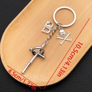 Silver punk keychain with cross, skull, and hollow book charms on a wooden tray