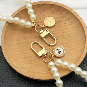 Faux pearl keychain with bow pendant and golden sunburst charm on wood tray