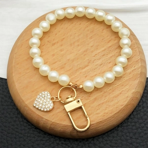 Elegant large pearl keychain with golden carabiner and rhinestone heart pendant on wood