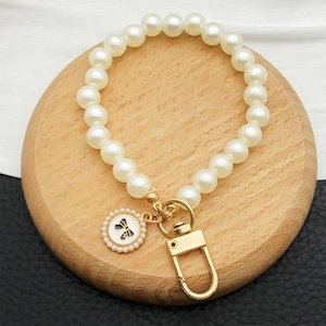 Detail of pearl keychain with gold clasp and black bow pendant on wooden stand