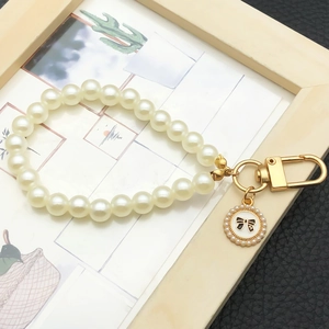 Detail of faux pearl keychain with gold metal clasp and S-letter bow pendant charm