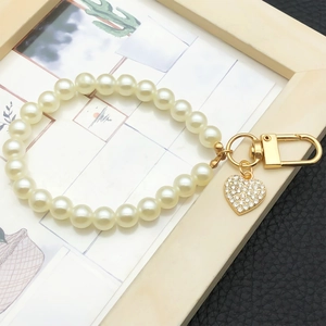 Detail of faux pearl keychain with a gold lobster clasp and a sparkling zircon heart pendant