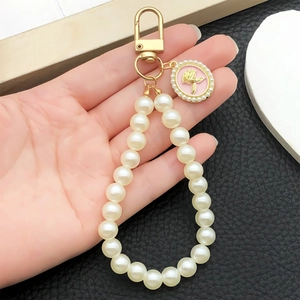 Pendentif rose en relief avec perles sur porte-clés doré tenu par une main