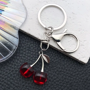Detail of red translucent cherry keychains with silver lobster clasp on leather background