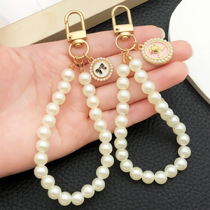 Hand holding a faux pearl bead keychain with golden rose and bow round charms