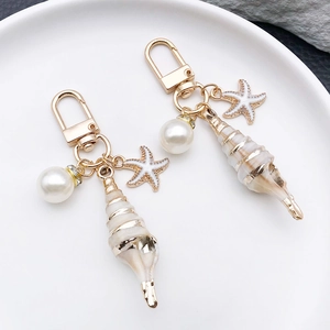 Detail of seashell and starfish keychains with pearls and gold accents on a white tray