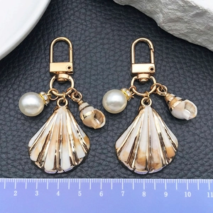 Golden ocean theme shell keychain with pearl and conch charms on black leather background